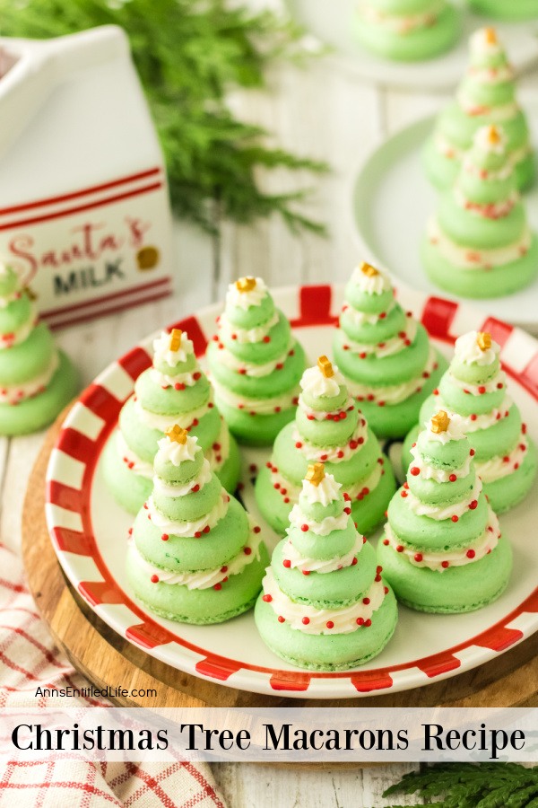 Christmas Tree Macarons Recipe – Festive Holiday Treats Overhead image of 8 Christmas tree macarons on a Christmas paper plate. There are two more in the upper right on a white plate. Another macaron sits un the upper left in from of a Santa's milk sign.
