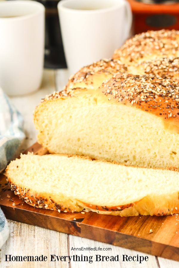 Profile view of a loaf of homemade everything bread on a wire rack a cutting board, several pieces are sliced away