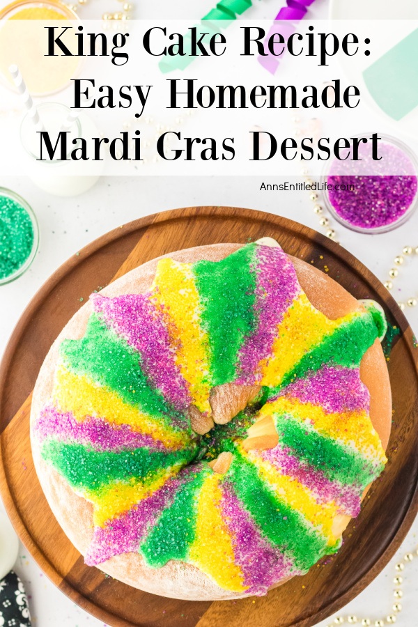 An overhead view of a whole king cake on a wooden server. There are beads and colored sugar above the platter.