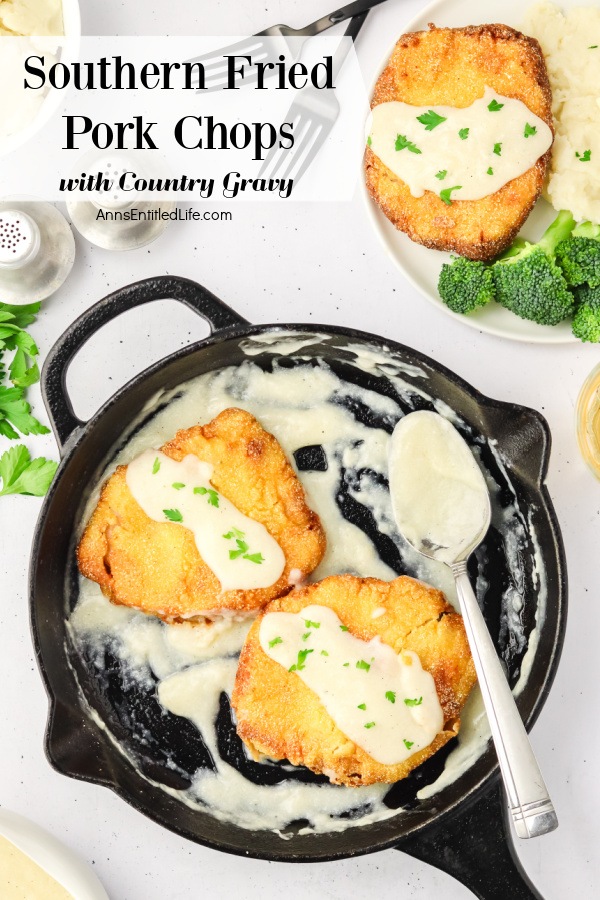 A cast-iron skilled with two southern fried pork chops covered in gravy, the spoon resting in the pan. In the upper right a white plate contains a pork chop, broccoli and potatoes. There is a salt and pepper shaker in the upper left.
